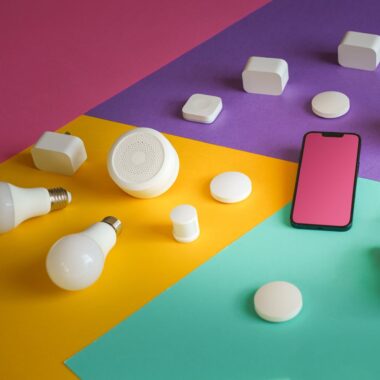 A vibrant display of smart home devices including bulbs, sensors, and a smartphone on a colorful background.