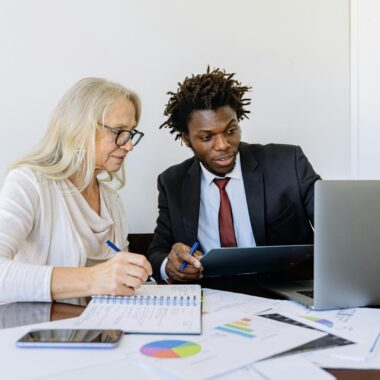 Two business professionals collaborating at a desk with laptops and documents in an office setting.